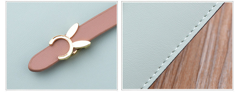Close-up of light blue wallet clasp with pink bow charm and stitched edge.