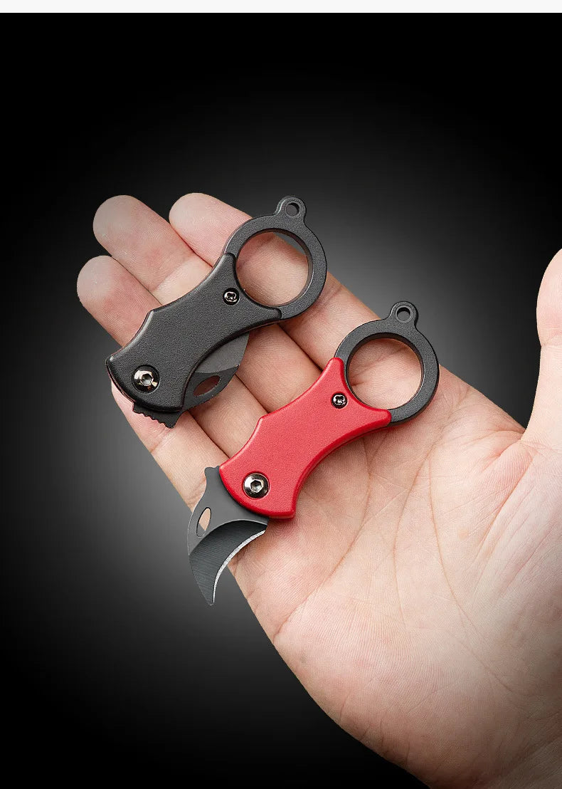 Mini folding pocket knife with keychain ring held in hand, red and black handles