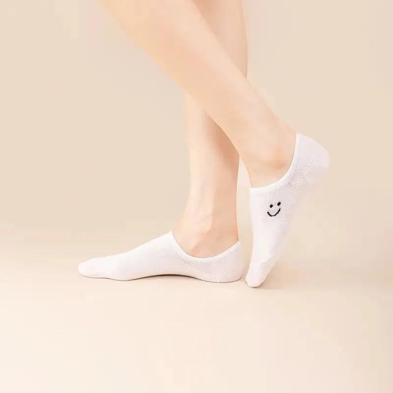 Women’s no-show low-cut socks in white with smiley face, worn on feet.