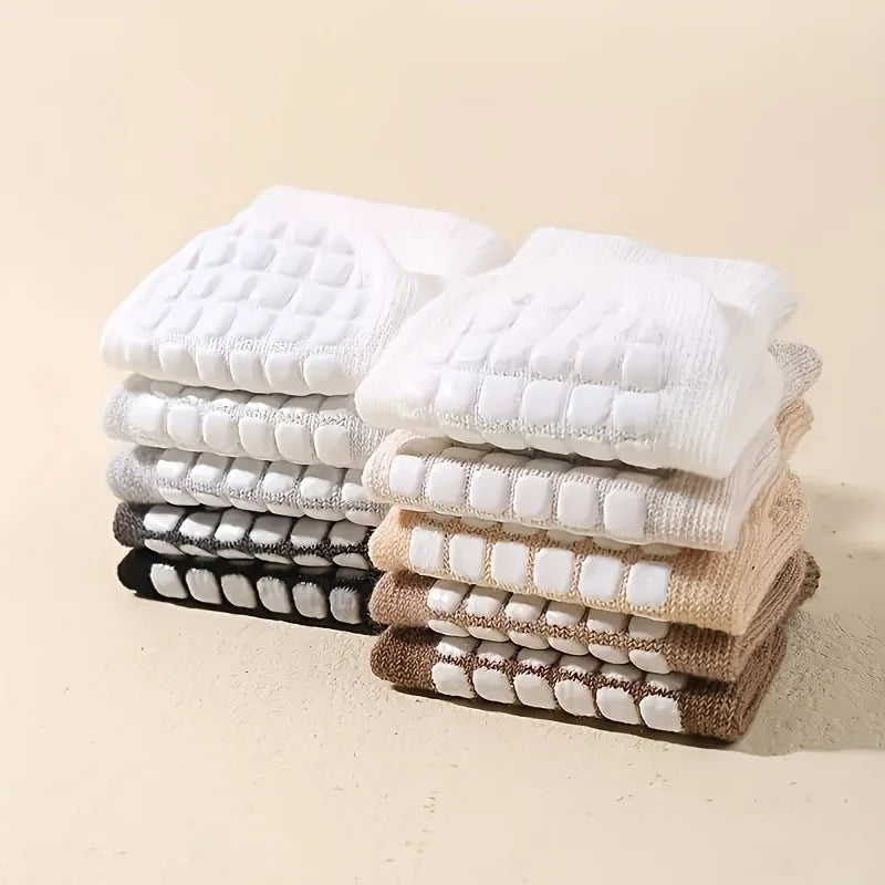 Stack of baby no-slip socks with grippy mesh soles in white, tan, and brown