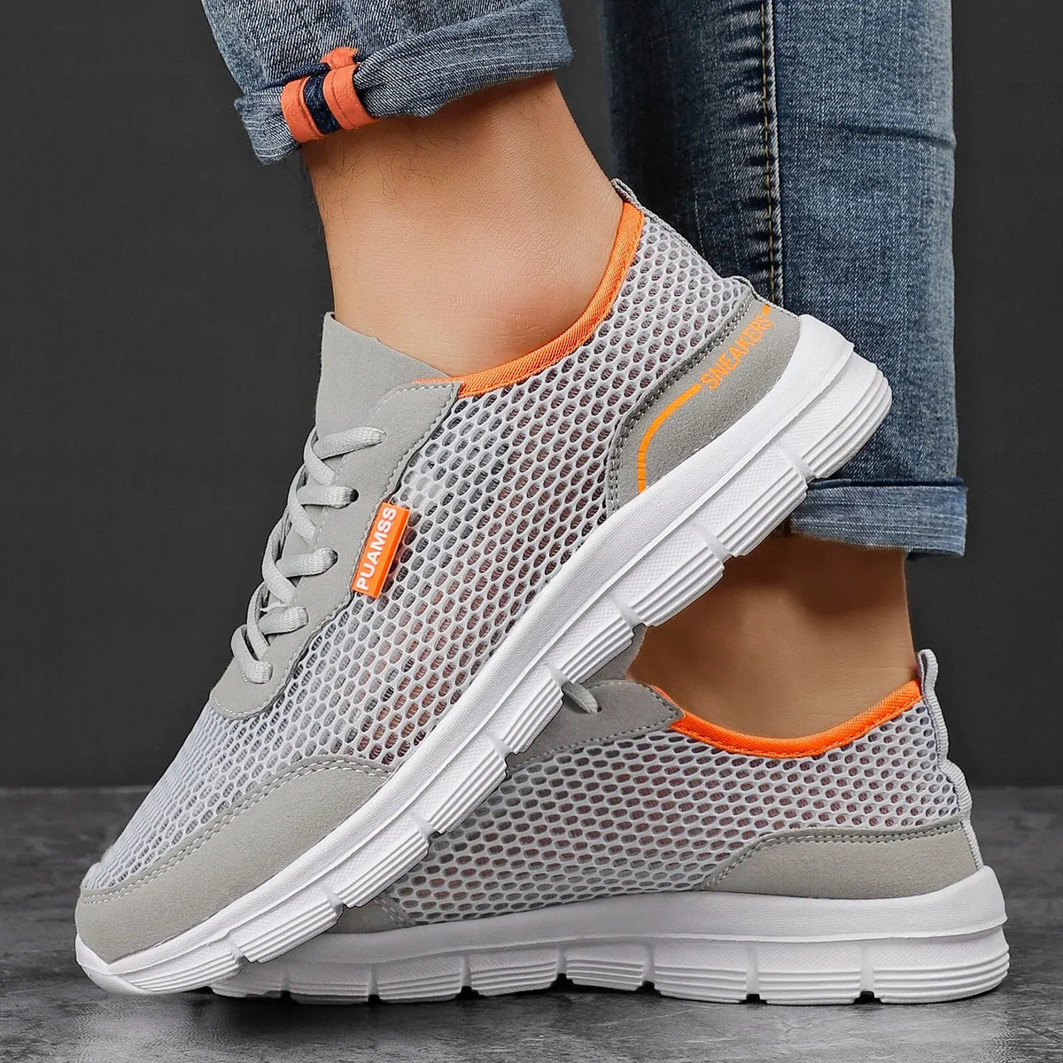 Men's sneakers on legs, gray mesh upper with orange trim, lace-up with white sole