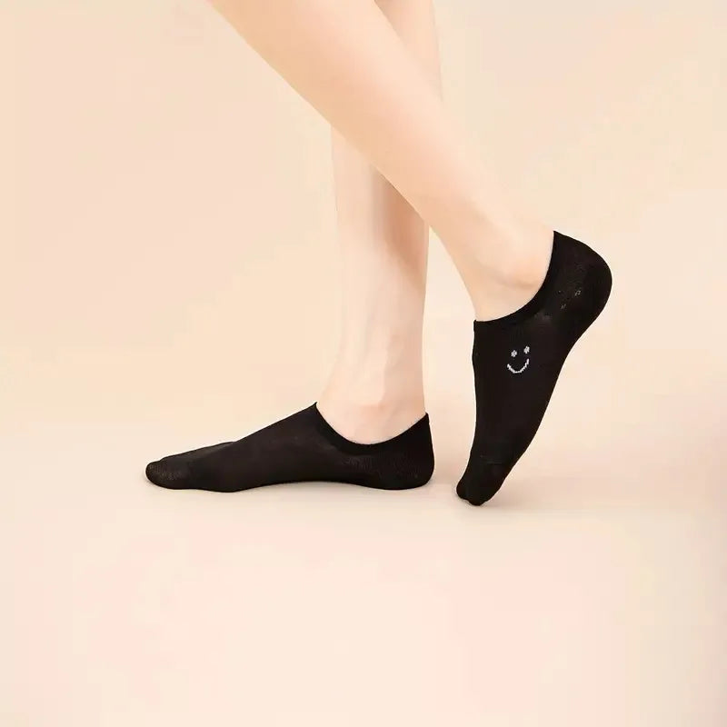 Women’s no-show low-cut socks in black with smiley face, worn on feet.