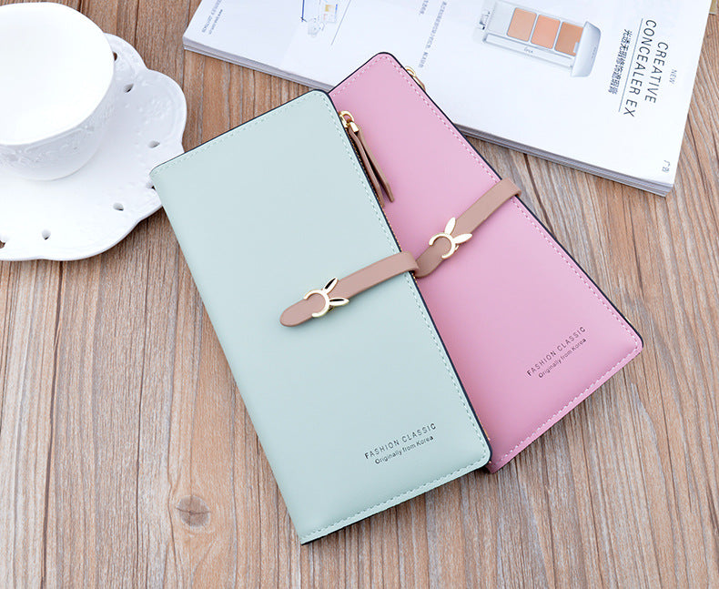 Long two-tone light blue and pink wallet purse with bow strap and gold zipper details.