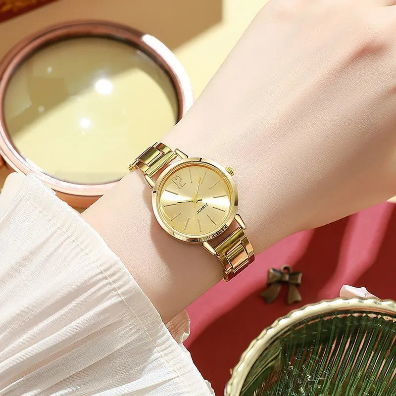 Women's quartz wristwatch with gold circular dial and metal link bracelet on wrist.