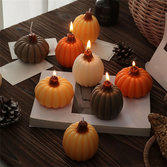 Pumpkin-shaped aromatherapy candle, lit wick; orange, white, and dark brown pumpkins.