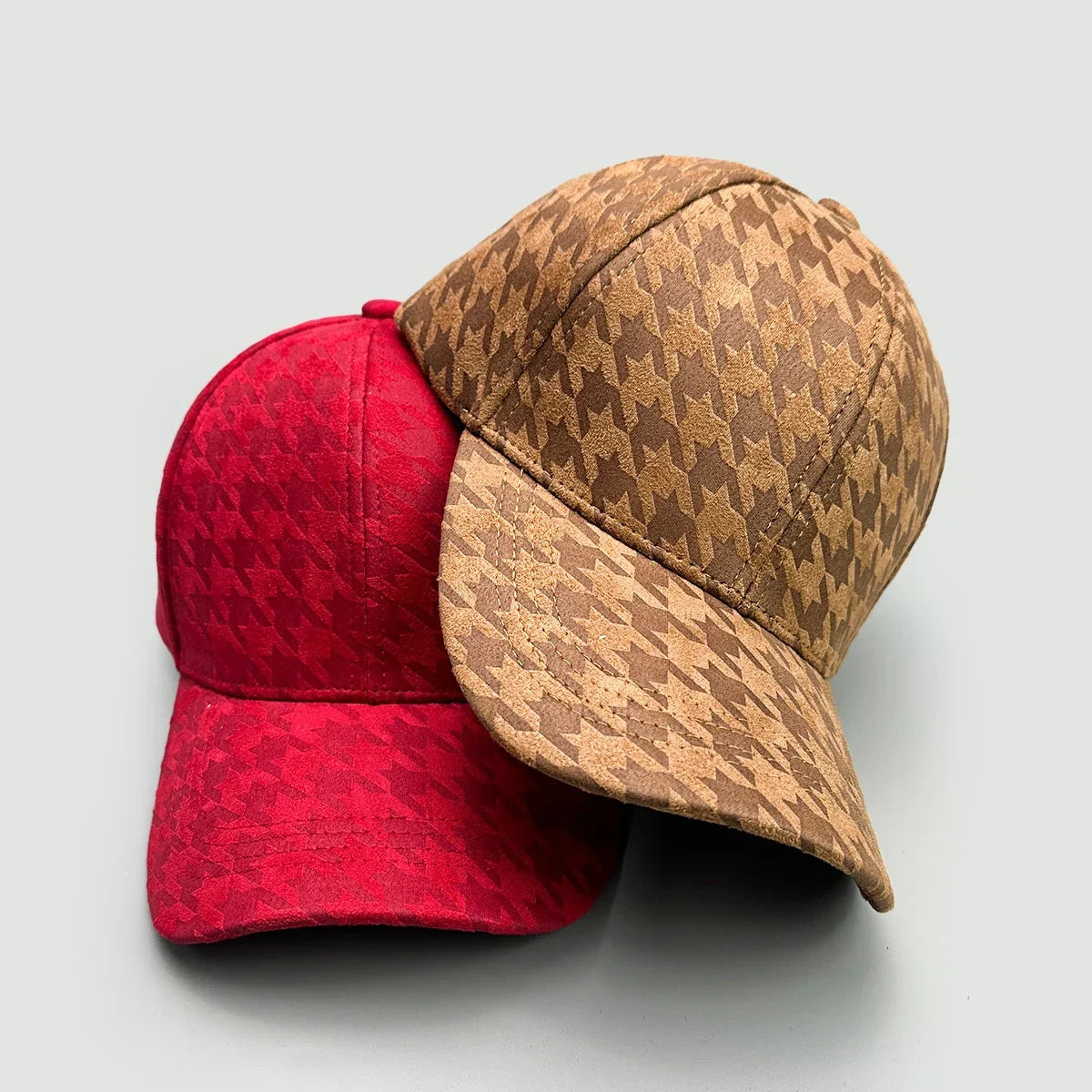 Two suede baseball caps with houndstooth patterns in red and tan colors.